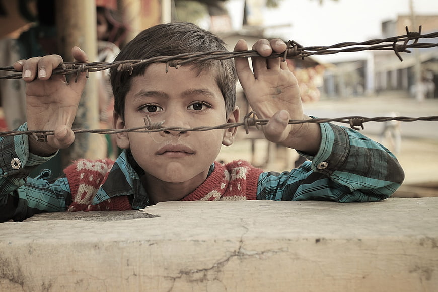 Portrait of young boy looking through barbed wire fence