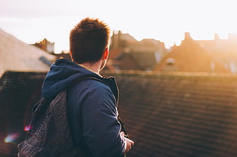Young Man with Backpack Looking at Rooftops at Sunset
