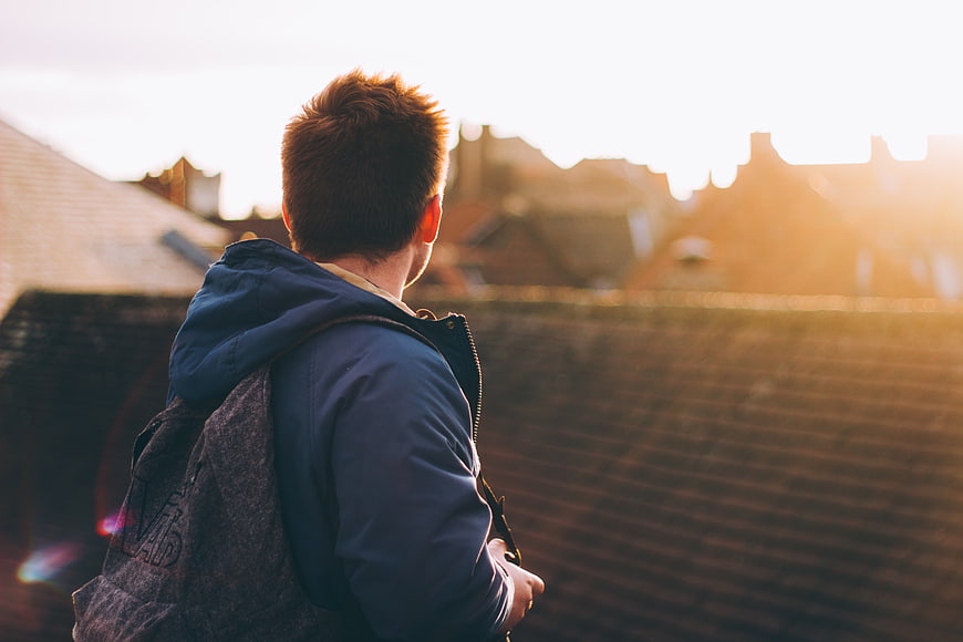 Young Man with Backpack Looking at Rooftops at Sunset