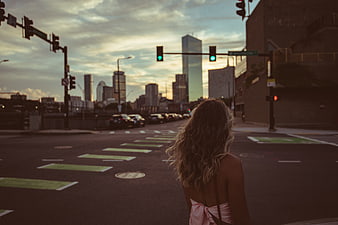 Woman with blonde hair walking on city street at sunset