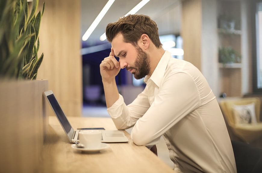 Stressed businessman rubbing temples at laptop in office