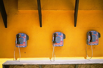 Three vintage payphones on a bright yellow wall