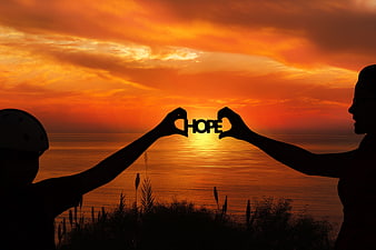 Silhouettes forming heart shape with word HOPE at sunset