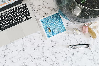 Flat lay workspace with laptop, glasses, and pineapple print on marble
