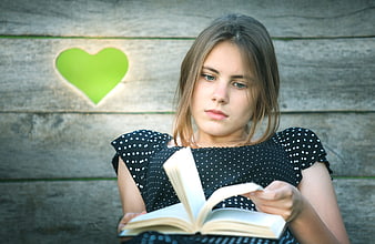 Young woman reading book against rustic wooden wall with green heart cutout