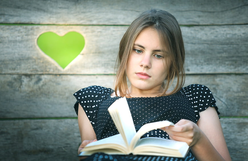 Young woman reading book against rustic wooden wall with green heart cutout