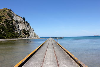 Concrete pier with railway tracks extending into calm blue ocean