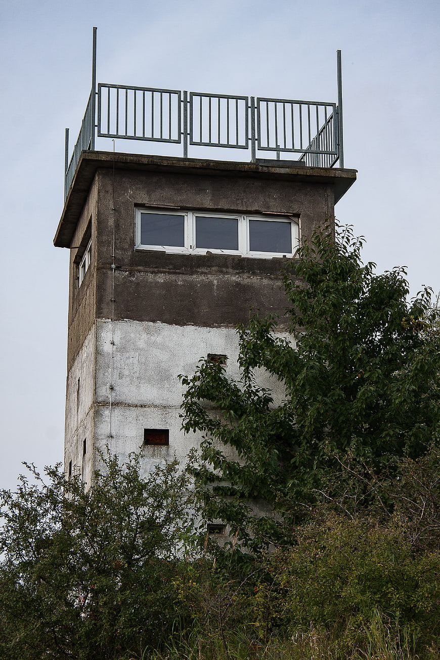 Abandoned concrete watchtower with overgrown vegetation
