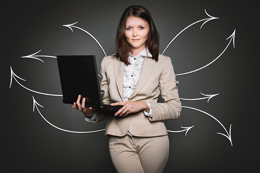 Businesswoman holding laptop with chalk arrows on blackboard background