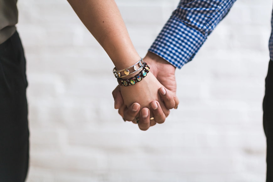 Couple Holding Hands with Bracelets Against White Wall