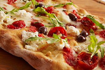 Close-up of rustic pizza with arugula, olives, and fresh cheese