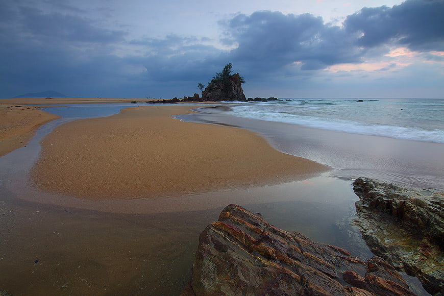 Dramatic coastal landscape with sandbar, rocks, and cloudy sky
