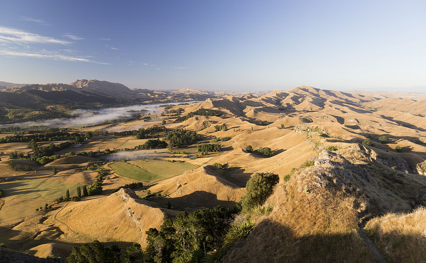 Golden rolling hills landscape with morning mist and blue sky