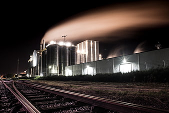 Industrial factory complex at night with smokestacks and railway tracks