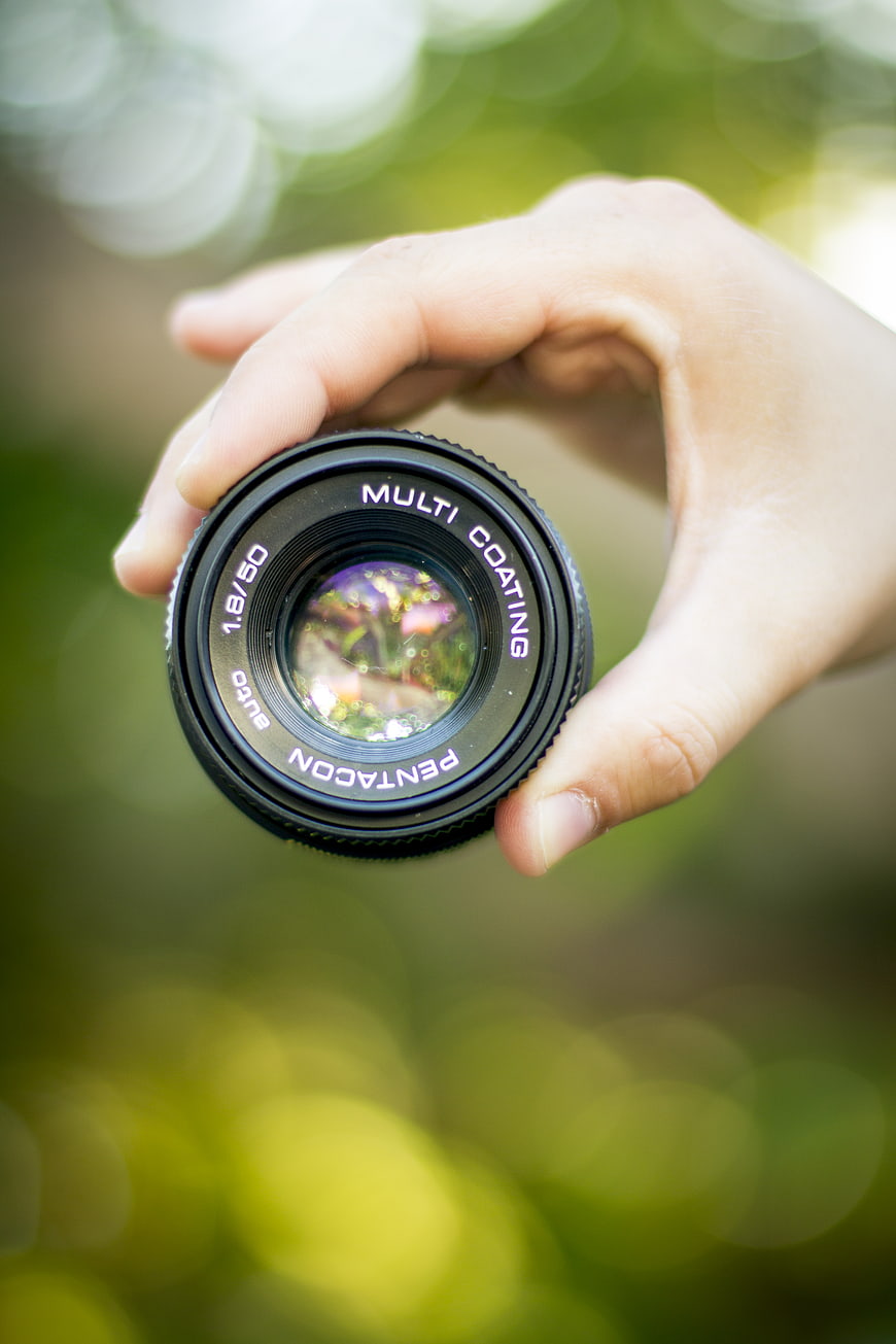 Hand holding Pentax camera lens with bokeh background