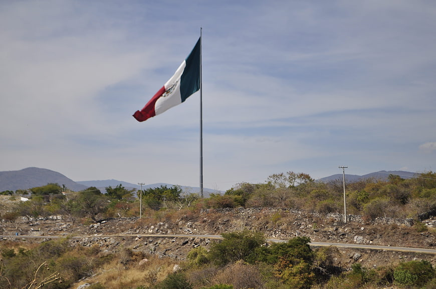 Mexican flag waving on a hillside against a blue sky