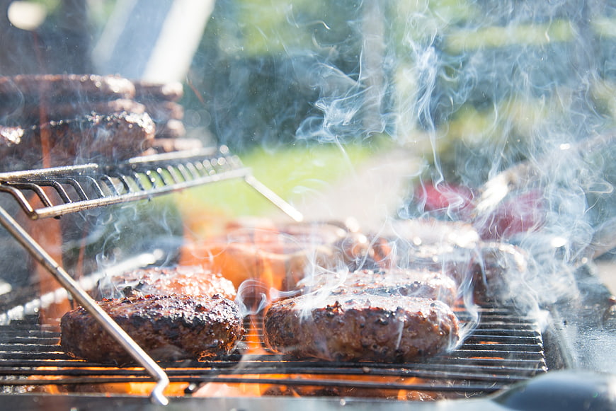 Sizzling burger patties grilling over open flames with smoke