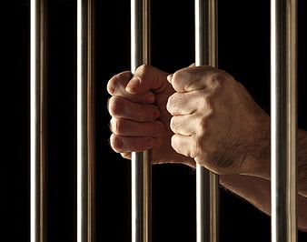 Hands gripping metal prison bars against black background