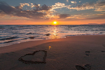 Heart drawn in sand on beach at sunset with ocean waves