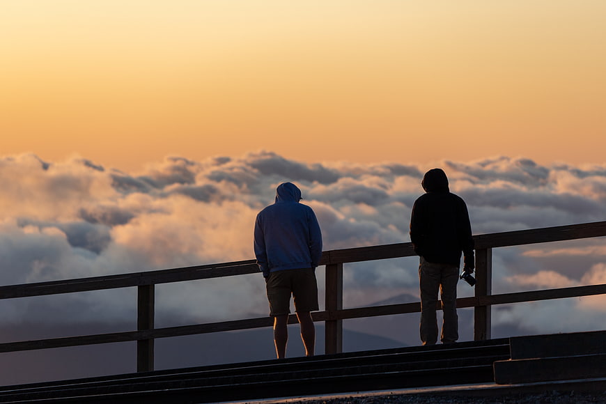 Silhouettes of Two People Watching Sunset Over Sea of Clouds