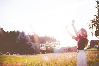 Woman with arms raised in field at sunset