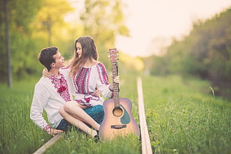 Young couple in traditional embroidered shirts sitting on railway tracks with guitar