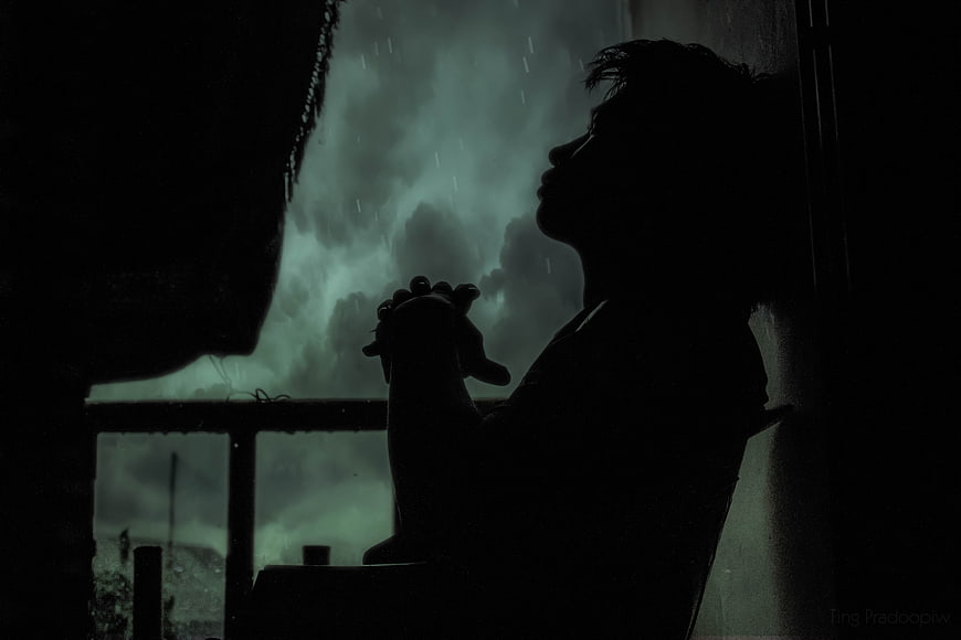 Silhouette of Boy Praying by Window in Rain