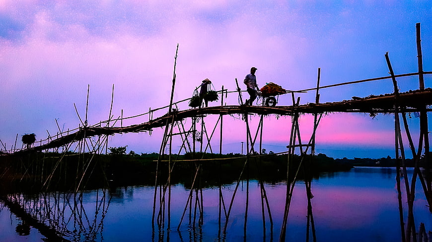 Silhouettes of people crossing a bamboo bridge at sunset