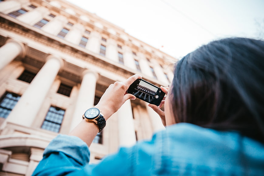 Woman photographing classical architecture with smartphone