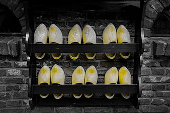 Yellow Dutch Wooden Clogs on Black Shelf Against Brick Wall