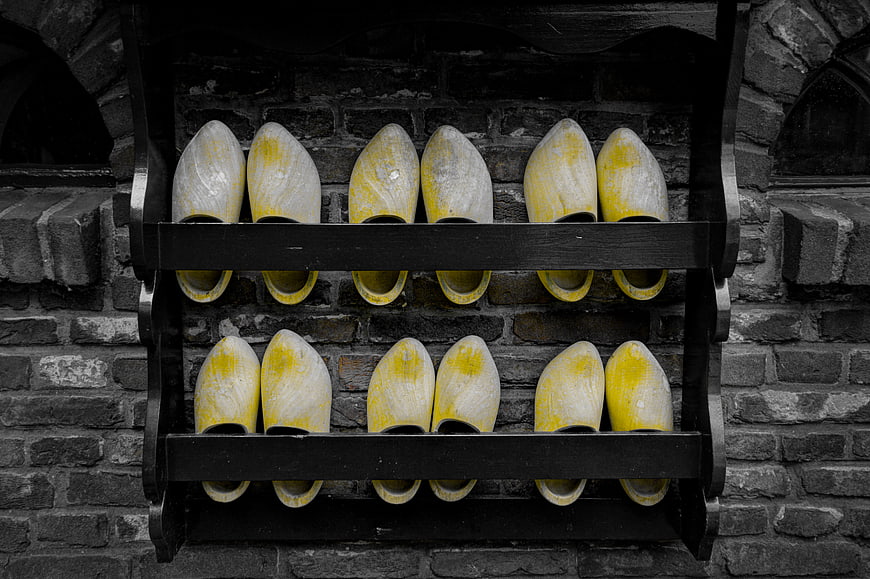 Yellow Dutch Wooden Clogs on Black Shelf Against Brick Wall