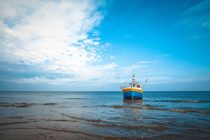 Blue and yellow fishing boat anchored in calm sea near sandy beach