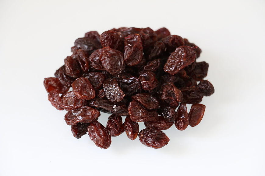 Pile of dark red dried raisins on a clean white background