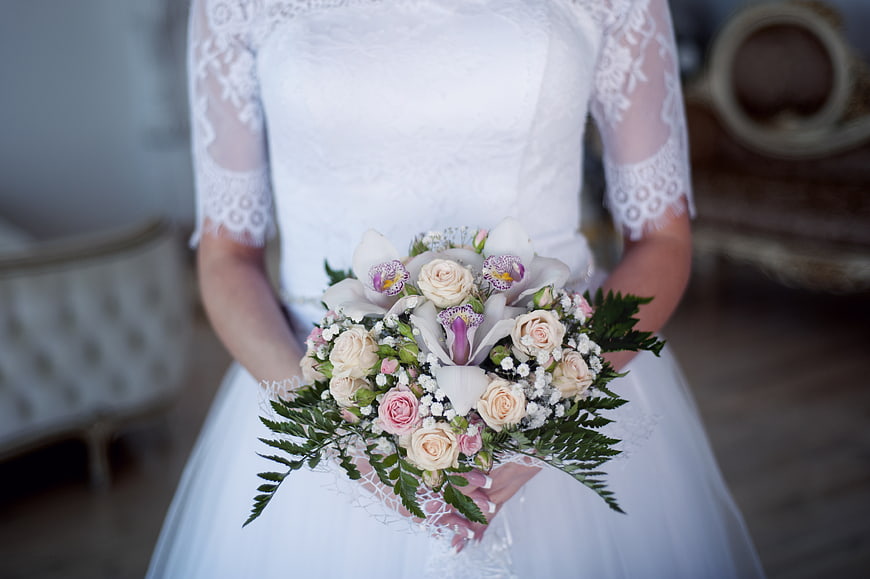 Bride holding elegant wedding bouquet with roses and orchids