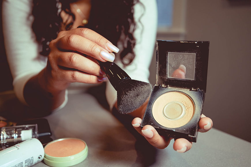 Woman applying makeup with brush and powder compact