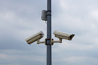 Dual Security Cameras on Metal Pole Against Cloudy Sky