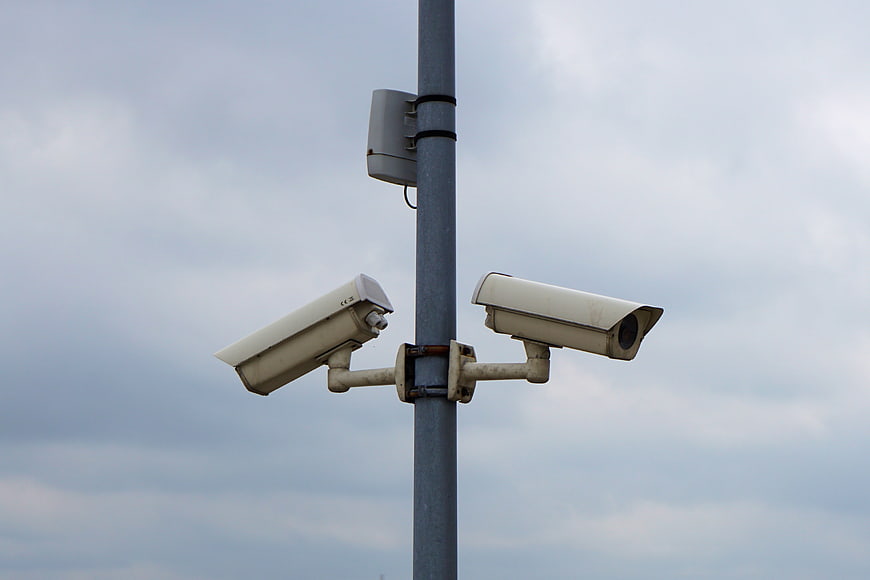 Dual Security Cameras on Metal Pole Against Cloudy Sky