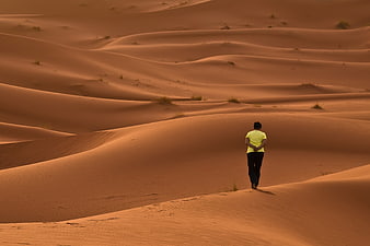 Man Walking Alone On Vast Orange Desert Sand Dunes