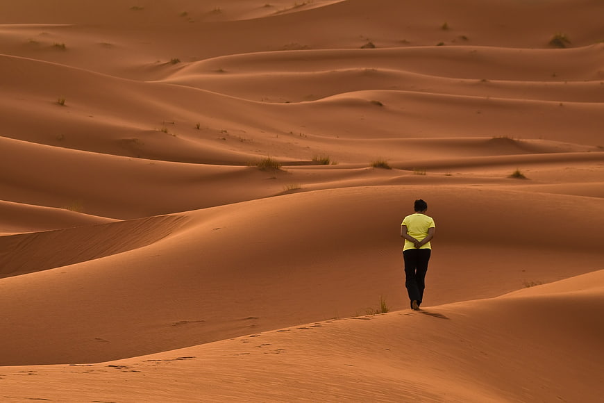 Man Walking Alone On Vast Orange Desert Sand Dunes