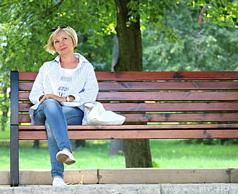 Senior blonde woman sitting on park bench looking away