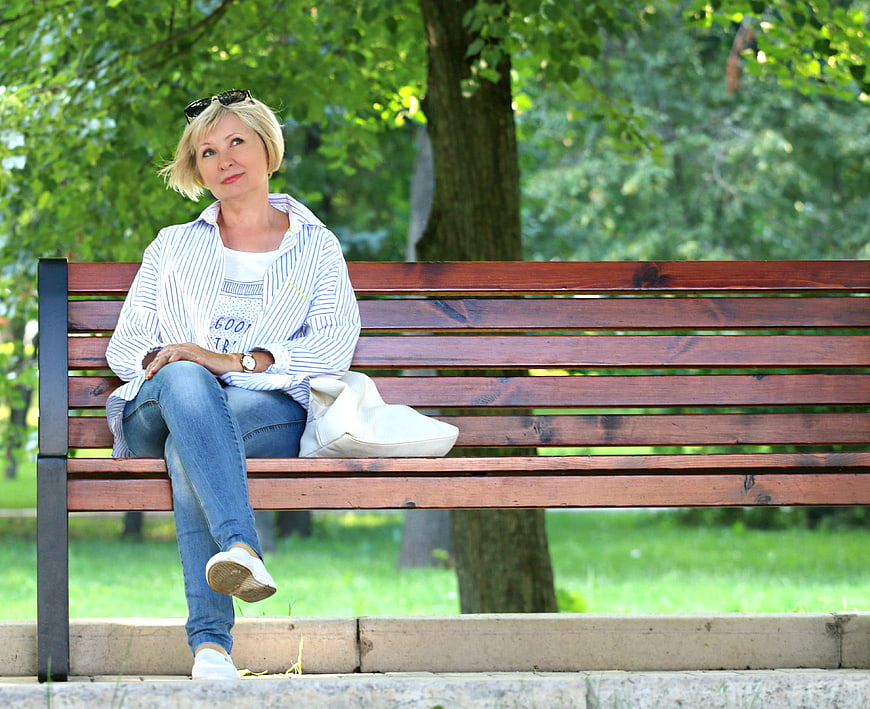 Senior blonde woman sitting on park bench looking away