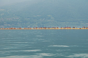 Crowd walking on floating bridge over blue lake
