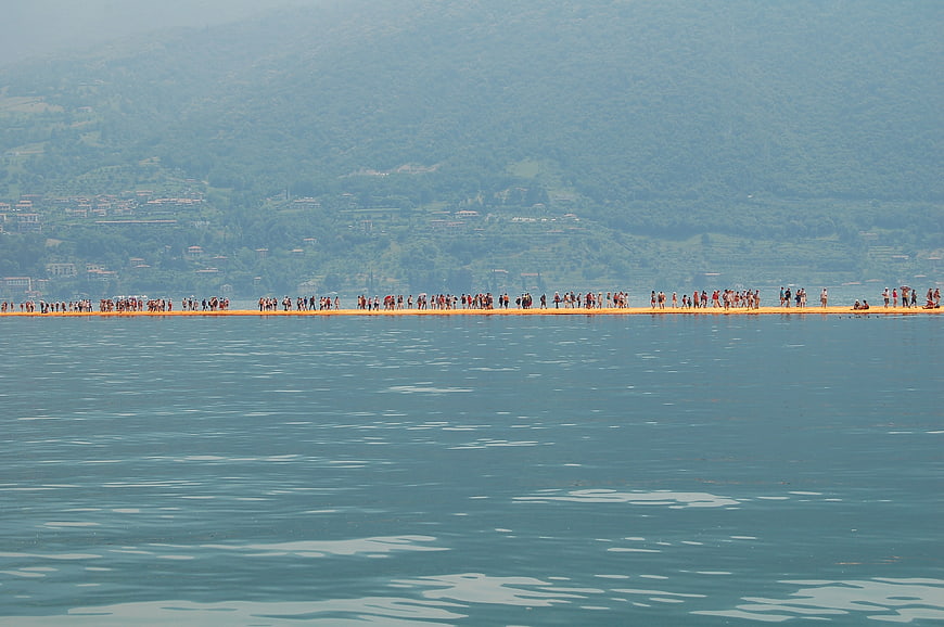 Crowd walking on floating bridge over blue lake