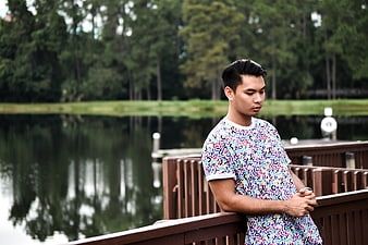 Young Man in Colorful Shirt Leaning on Wooden Dock by Lake