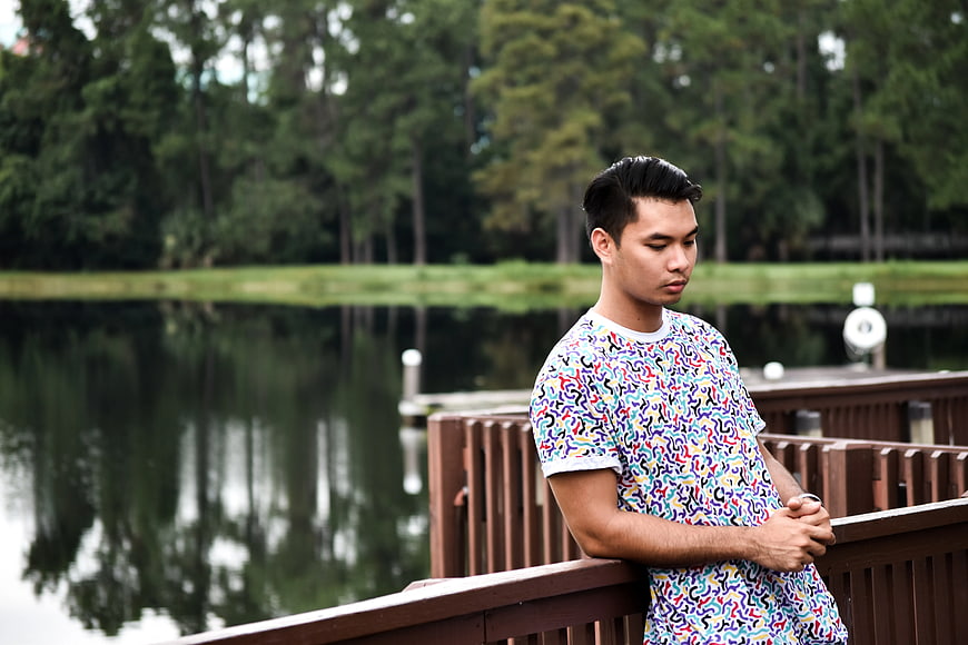 Young Man in Colorful Shirt Leaning on Wooden Dock by Lake