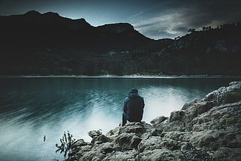 Man sitting on rocks by a misty lake at dusk