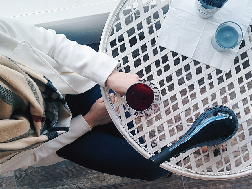 Top view of woman holding red wine glass on white table
