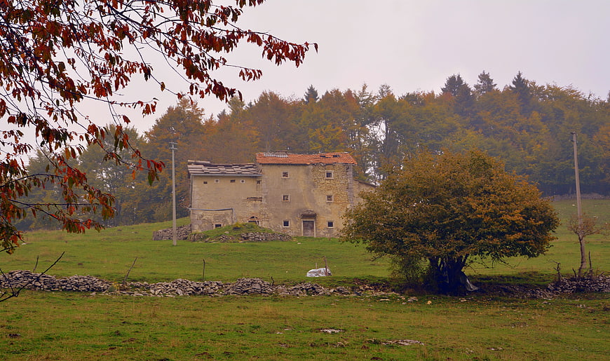 Old stone farmhouse in autumn landscape with red leaves