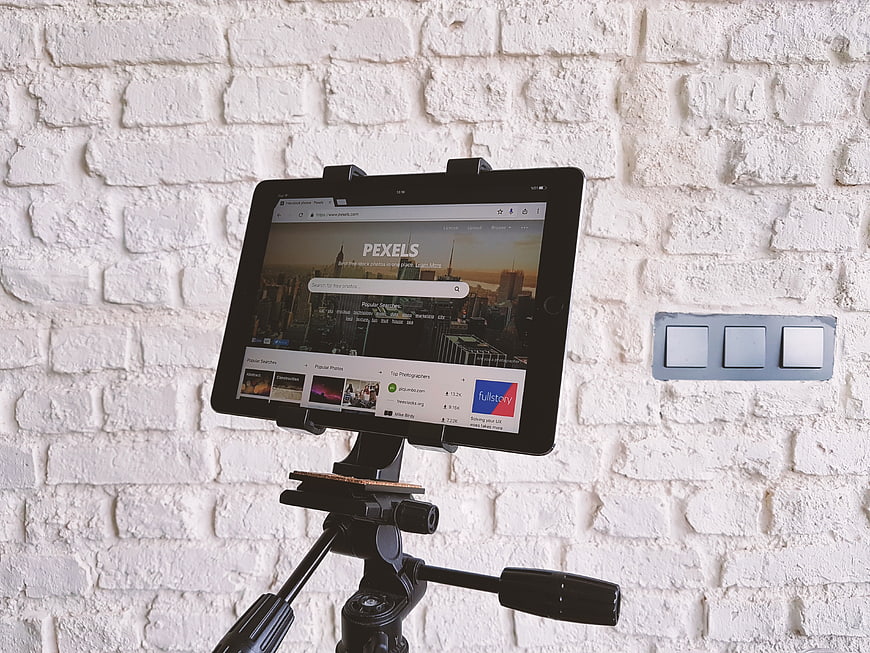 Tablet on Tripod Displaying Pexels Website Against White Brick Wall