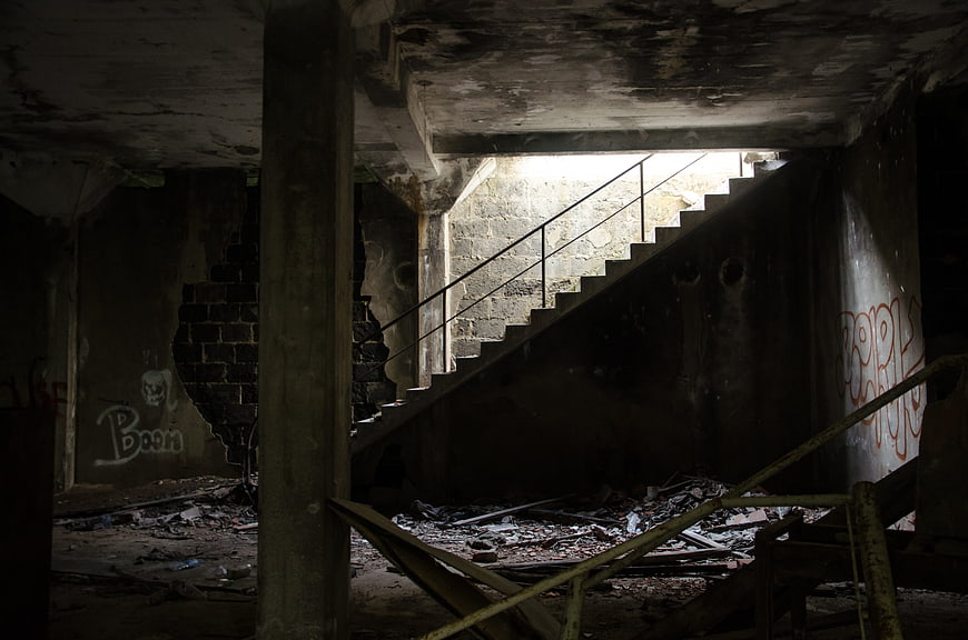Dark abandoned staircase in dilapidated concrete building with graffiti